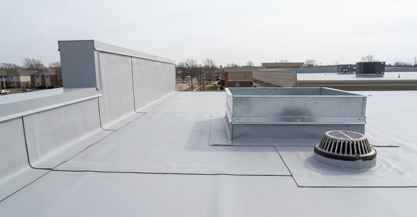 A white low-slope commercial roof membrane with a metal parapet edge and a round roof drain.